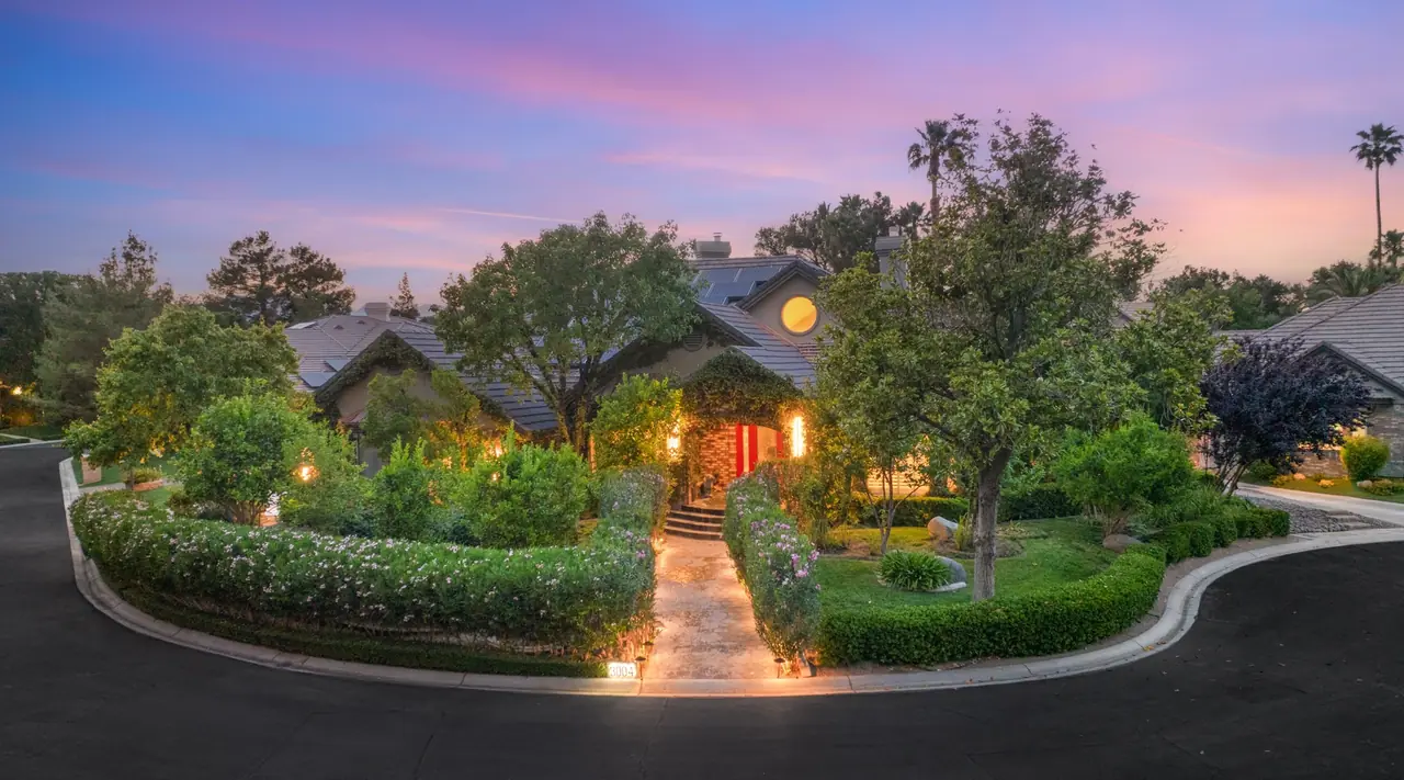 Front of the home at dusk with lit landscaping and circular drive